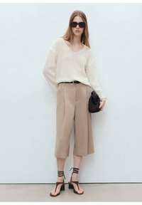 Beige wide-leg pants, ivory textured sweater, black belt, strappy brown sandals, black handbag, oversized sunglasses, minimalistic background.