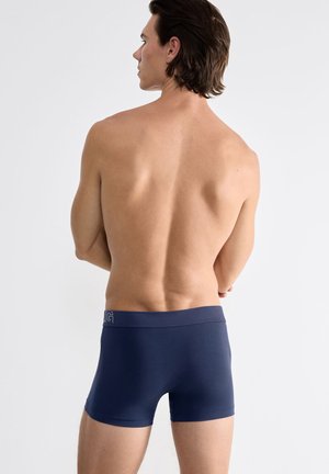 Marineblaue Boxer-Shorts aus elastischem Stoff, mit einem breiten elastischen Bund und einem Logo-Detail auf der Vorderseite.
