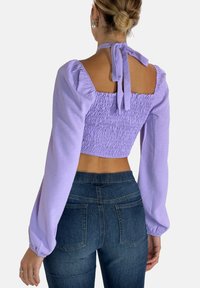 Lilla crop top med smocket ryg, puffede ærmer og knytning ved halsen. Sættes sammen med mørkeblå højtaljede jeans.