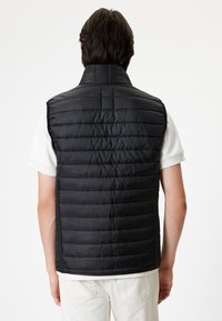 Gilet isolato nero con colletto alto e design a trapunta orizzontale, caratterizzato da una texture liscia e una silhouette aderente, indossato su una camicia bianca.