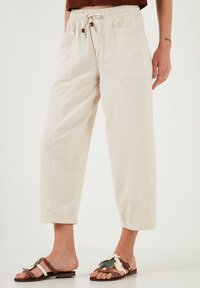 Light beige wide-leg pants in a textured fabric, featuring an elastic waistband with drawstrings. Paired with decorative sandals.