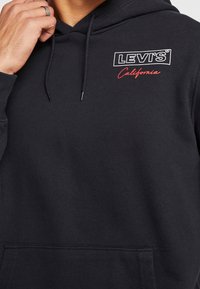 Sudadera con capucha negra hecha de una mezcla de algod ón. Presenta un bolsillo frontal, cordón, logotipo "LEVI'S" y "California" en cursiva roja.
