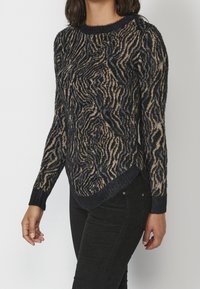 Jersey de punto en azul marino con un patrón texturizado de olas en beige. Presenta un cuello redondo y mangas largas, con puños y dobladillo acanalados.