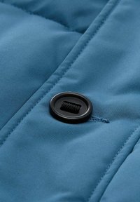 Modra puffer jakna iz materiala z gladko teksturo, z črnimi gumbki in šivanjem ob kvadratnih delih.