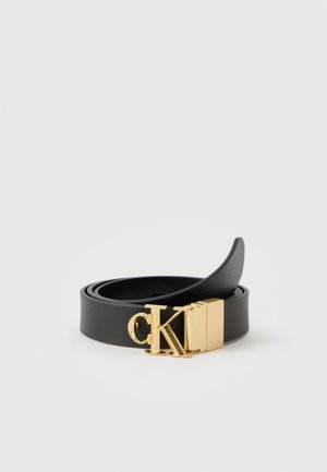 Czarny skórzany pasek zwinięty z złotą metalową klamrą z logo "cK" na białym tle.