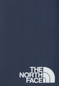 Tissu bleu foncé avec un motif de grille subtil, comportant le texte blanc "THE NORTH FACE" et le logo du demi-dôme dans le coin inférieur droit.