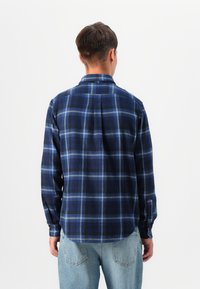 Blue and black plaid shirt with long sleeves and a collar, made from soft fabric, featuring a straight hem and buttoned cuffs.