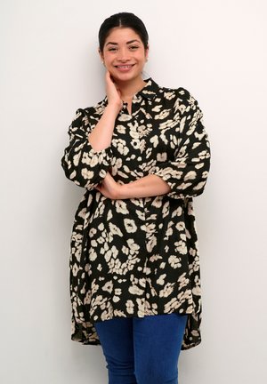 Sort skjorte med knapåbning og hvidt blomstermønster, afslappet pasform og lange ærmer, parret med blå jeans. Kantens længde er længere bagtil.