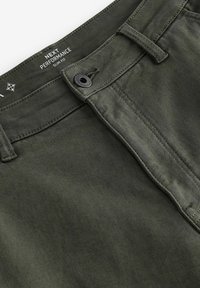 Schmale grüne Chinos aus glattem Stoff mit Knopfschluss und Gürtelschlaufen, versehen mit dezenten Nähten und Logo auf dem Taillenbund.