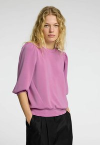 Pullover rosa con scollo tondo, maniche corte a sbuffo e vestibilità rilassata. Realizzato in un tessuto morbido e liscio. Abbinato a pantaloni neri.