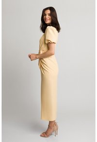 Żółta midi sukienka z bufkami, z paskiem w talii i gładką teksturą. Noszona z beżowymi sandałami na obcasie. Prosty i dopasowany fason.