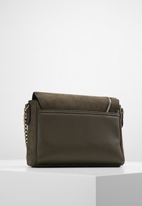 Olivgrüne Umhängetasche mit einer strukturierten Wildlederklappe, Lederkörper, goldener Kettenriemen und einer Reißverschlusstasche vorne.