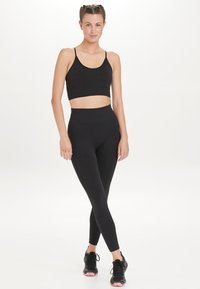 Zwarte crop top en high-waisted leggings, beide gemaakt van rekbaar materiaal. Gepaard met zwarte sportschoenen met een gemusterde zool.