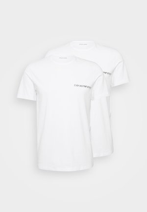 T-shirt in cotone bianco, colletto tondo, maniche corte, con un logo nero sul lato sinistro del petto. Due magliette esposte insieme.
