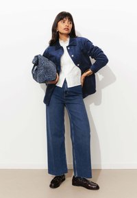 Veste en velours côtelé bleu sur un blouse en dentelle blanche, associée à un jean en denim taille haute et des mocassins noirs. Tient un sac à motifs léopard bleu.