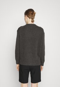 Mörkgrå stickad tröja med rund hals, raglanärmar och lös passform, tillsammans med svarta shorts, sedd bakifrån.