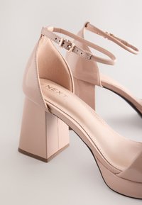 Lyserøde laklæder sandaler med høje hæle, firkantet blokhæl, ankelrem og spænde lukning. Glat tekstur og minimalistisk design.