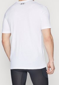 Camiseta blanca de manga corta con cuello redondo y un pequeño logo negro en la parte superior de la espalda. La tela parece ligera y suave.