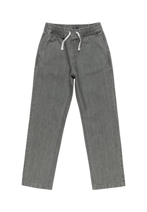 Brun bomulds T-shirt med korte ærmer og et rundt sort og hvidt bølgemotiv på brystet, parret med grå bukser og sorte sneakers.