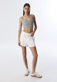 Top de tirantes corto color gris claro con embellishments de perlas, pantalones cortos blancos con cordón, y zapatillas blancas con detalles gráficos en rosa.