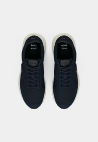 Σκούρα μπλε αθλητικά παπούτσια με υφαντό πάνω μέρος, σχέδιο με κορδόνια και μαλακή εκρού σόλα. Εμφανές λογότυπο στη γλώσσα και στο πλάι.