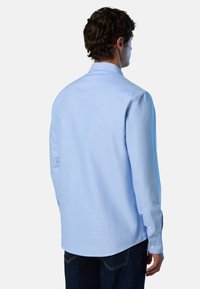 Camicia azzurro chiaro a maniche lunghe in cotone, con colletto classico, polsini con bottoni e orlo curvo. Tessuto liscio e design aderente.