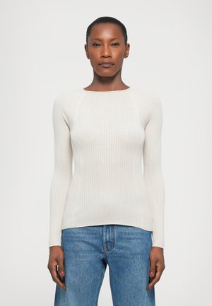 Lys beige ribbet langermet topp med rund hals og tettsittende silhuett, kombinert med blå denim jeans. Glatt tekstur og stretch.