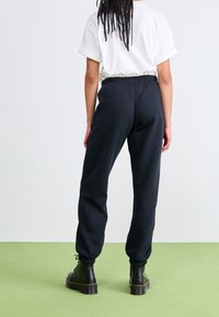 Schwarze Jogginghose aus weichem Stoff mit elastischem Bund und Bündchen. Kombiniert mit schwarzen Schnürstiefeln, Rückansicht.