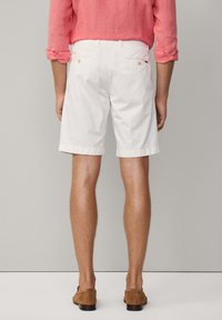 Pantaloni corti bianchi in cotone con taglio dritto, tasche laterali e tasche posteriori. Presentano anche un orlo arrotolato e scarpe in suede color beige.