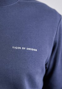 Felpa blu navy realizzata in tessuto morbido, con il logo bianco "TIGER OF SWEDEN" sul petto. Design casual con scollatura tonda.