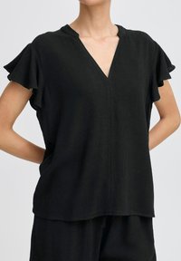 Top nero a maniche corte con scollatura a V, maniche arricciate e vestibilità comoda. Realizzato in tessuto leggero con una texture liscia.