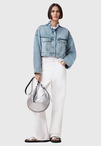 Chaqueta de denim recortada con cuello deshilachado, cierre de botones y dos bolsillos frontales; combinada con pantalones anchos blancos y un bolso metálico plateado.