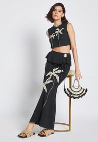Completo nero composto da un top corto con ricami di palme e una gonna svasata con vita peplum, abbinato a sandali beige e una borsa di perline.