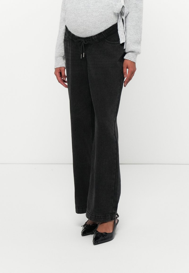 Calças de denim pretas de perna larga com cintura elástica e detalhe de cordão, combinadas com sapatos pretos de bico fino.