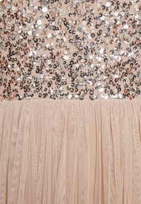 Tissu embellis de sequins avec des teintes rose doré et argent, présentant un bustier en maille nude texturée et une jupe en tulle superposée.