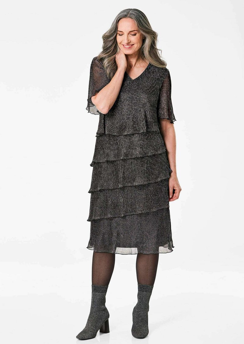 Robe noire à volants avec un tissu texturé et scintillant. Décolleté en V, manches courtes et longueur cheville. Assortie à des bottes à talons grises.