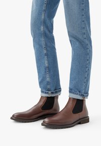 Bruna läder Chelsea-stövlar med elastiska sidopaneler, texturerad yta och en robust gummisula. Bärs med uppvikta ljusblå jeans.