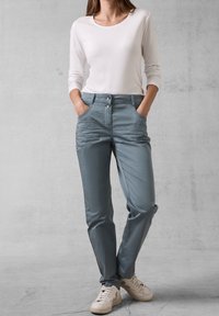 Jasnoszare, lekkie spodnie o gładkiej fakturze, z dwoma przednimi kieszeniami, dwoma guzikami i dopasowanym krojem, w połączeniu z białą bluzką z długim rękawem.