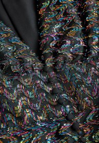 Fekete szövet színes, cikkcakk hímzéssel. Fényes felület, texturált részletek és fekete gombok jellemzik. Bonyolult varrásminták láthatók.