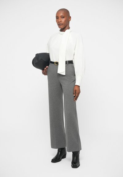White blouse with a neck tie, grey wide-leg trousers, black belt, and black bag. Model wears black ankle boots. Simple, clean design.