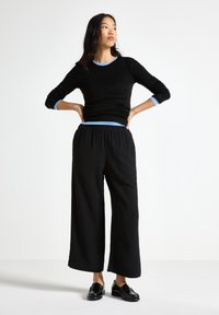 Top negro de manga larga con detalles en azul y pantalones negros de pierna ancha, combinados con zapatos negros. Tejido suave, ajuste relajado, diseño sencillo.