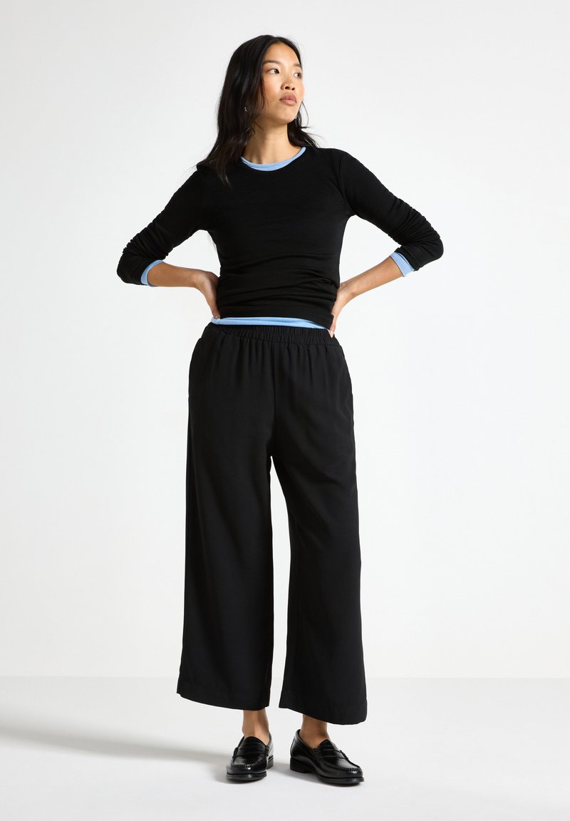 Top negro de manga larga con detalles en azul y pantalones negros de pierna ancha, combinados con zapatos negros. Tejido suave, ajuste relajado, diseño sencillo.