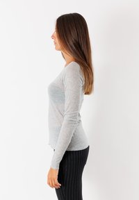 Maglia a maniche lunghe grigia chiara a coste con scollo tondo, abbinata a pantaloni neri a righe. Il tessuto sembra morbido e aderente.