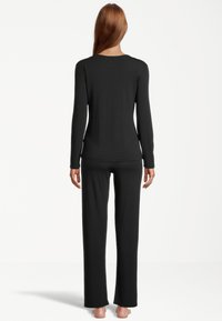 Schwarzes Langarmoberteil und passende Hose, aus glattem, dehnbarem Stoff. Das Design ist figurbetont, mit minimalen Nähten und einem schlichten Schnitt.