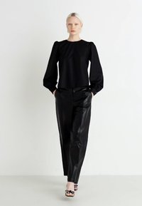Blusa nera a maniche lunghe con spalle arricciate, abbinata a pantaloni in pelle nera e tacchi aperti con motivo. Tessuto liscio, vestibilità sartoriale.