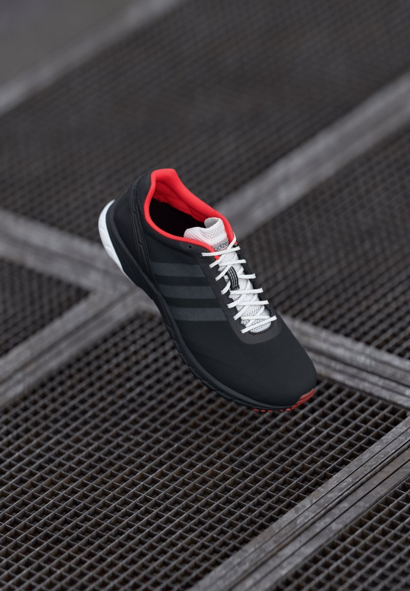 Black athletic shoe with red accents, white laces, and grey stripes. Features a textured upper and a cushioned sole for support.