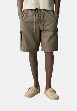 Pantaloni cargo marroni con una cintura elastica regolabile, tasche laterali e vestibilità sartoriale, abbinati a scarpe beige slip-on.