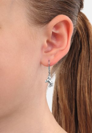 Orecchini d'argento con un ciondolo a forma di cavallo, caratterizzati da un design dettagliato e appesi a una chiusura ad uncino, indossati all'orecchio di un modello.