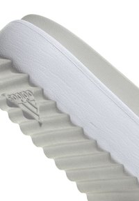 Adidas sportbačių padas, tekstūruotas guminis, šviesiai pilkas su banguota raštu, su iškilniu logotipu ir lygiu viršutiniu kraštu.
