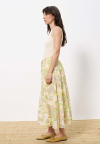 Hellbeige rippstrickärmelloses Top, kombiniert mit einem langen, floral bedruckten Rock in Pastellfarben. Dazu gehören flache, goldfarbene Schuhe.